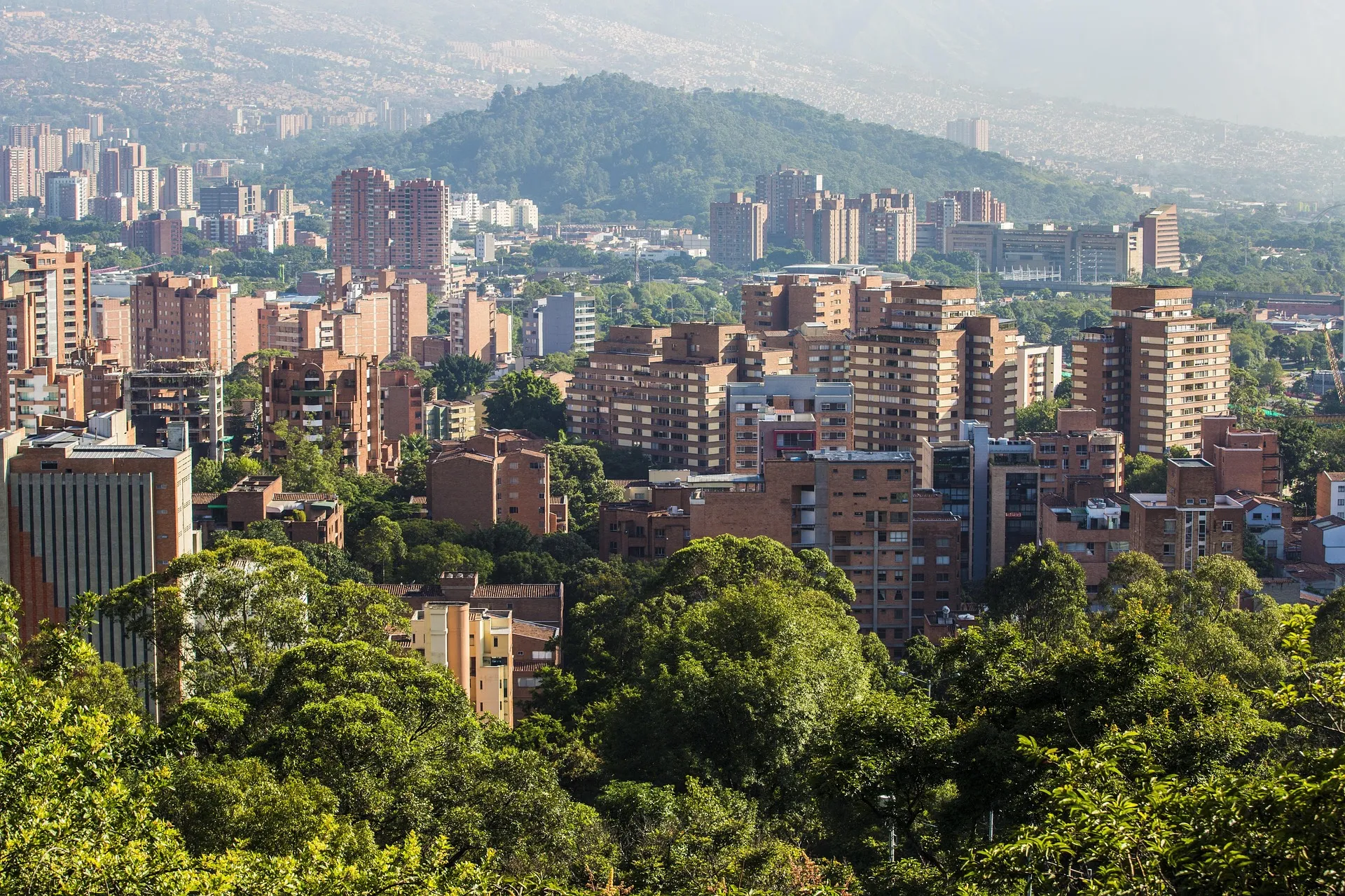 Laureles residencial e arborizado, Medellín — torres de tijolo vermelho entre árvores verdes na hora dourada