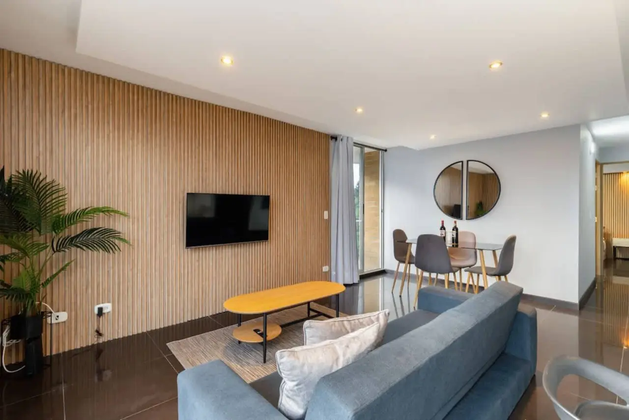 Casa Palmas — the living room under its wood-slat wall, opening to the balcony, San Diego, Medellín