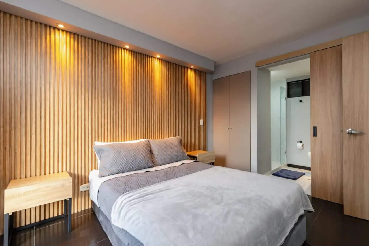 The main bedroom against its wood-slat wall, with the bathroom door beside the bed
