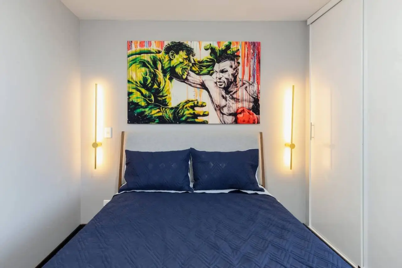 The second bedroom's blue bed between two wall lights, under the artwork