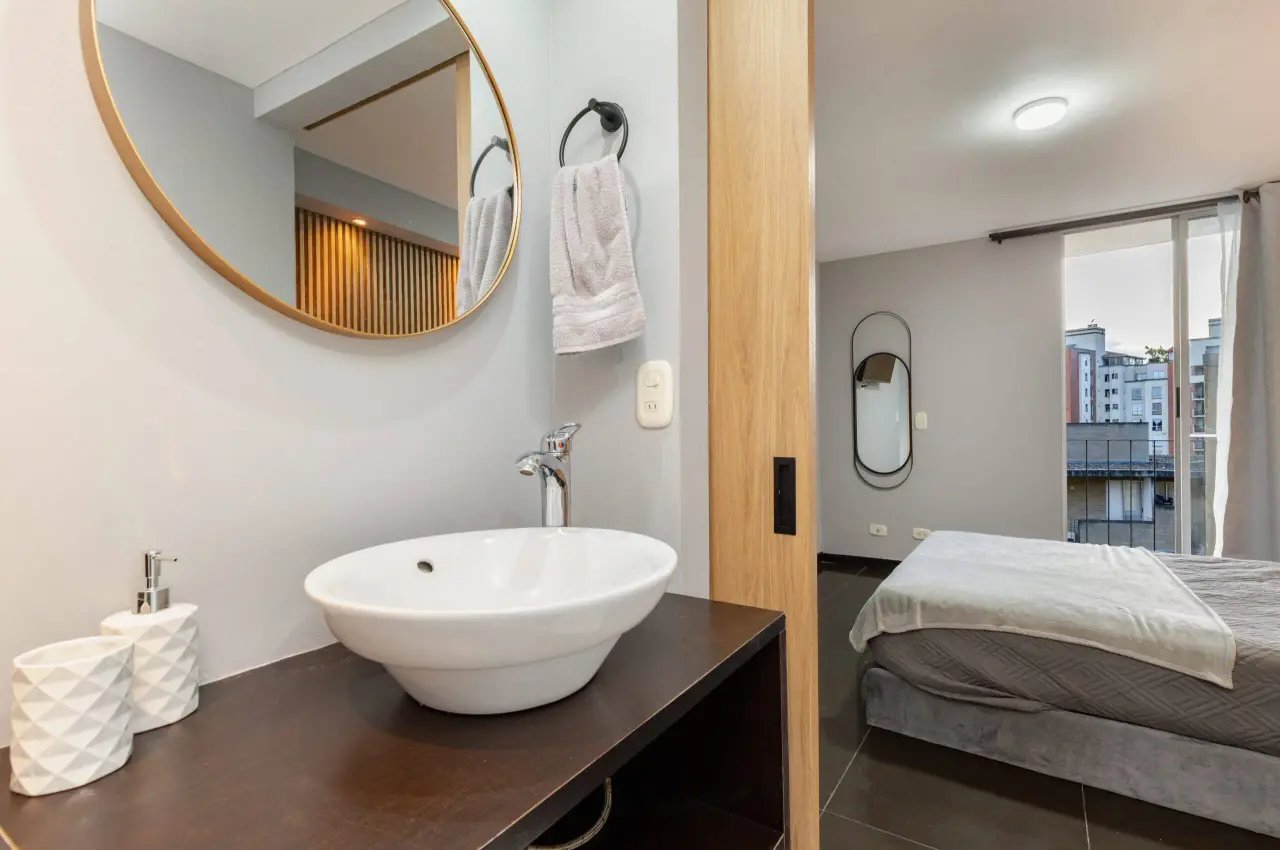 Bathroom with a vessel basin and round mirror, open to the bedroom