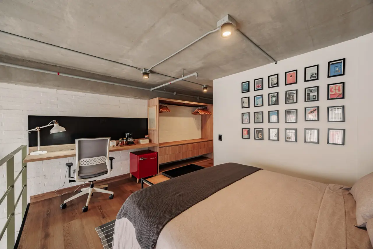 Mezzanine bedroom with a gallery wall of prints, a desk and a chair under the concrete ceiling