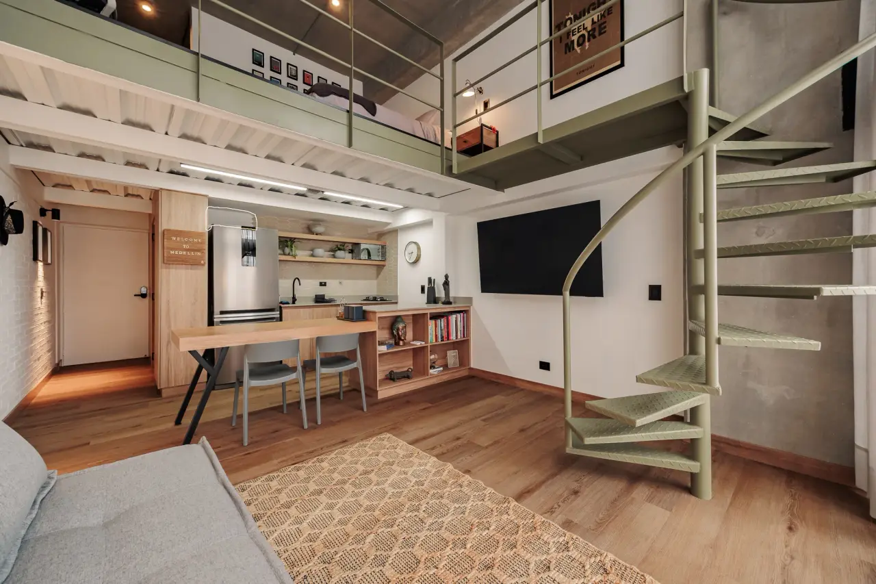 The loft seen end to end — dining, kitchen and the mezzanine bedroom above, behind a two-story wall of glass