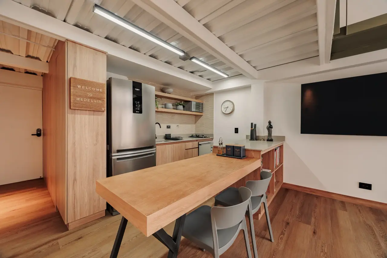 Long dining table for four with the kitchen and the TV wall behind it