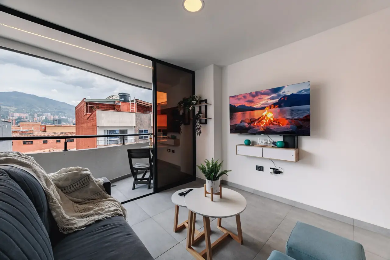 Living room with a wall TV and the glass doors open to the balcony and the mountains