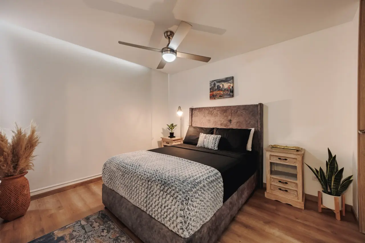 Main bedroom with a padded headboard, two nightstands and a ceiling fan
